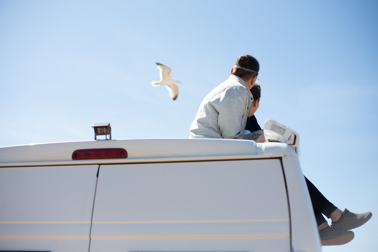 Couple enjoying a sunny day sitting on van roof with a seagull above in Portugal.