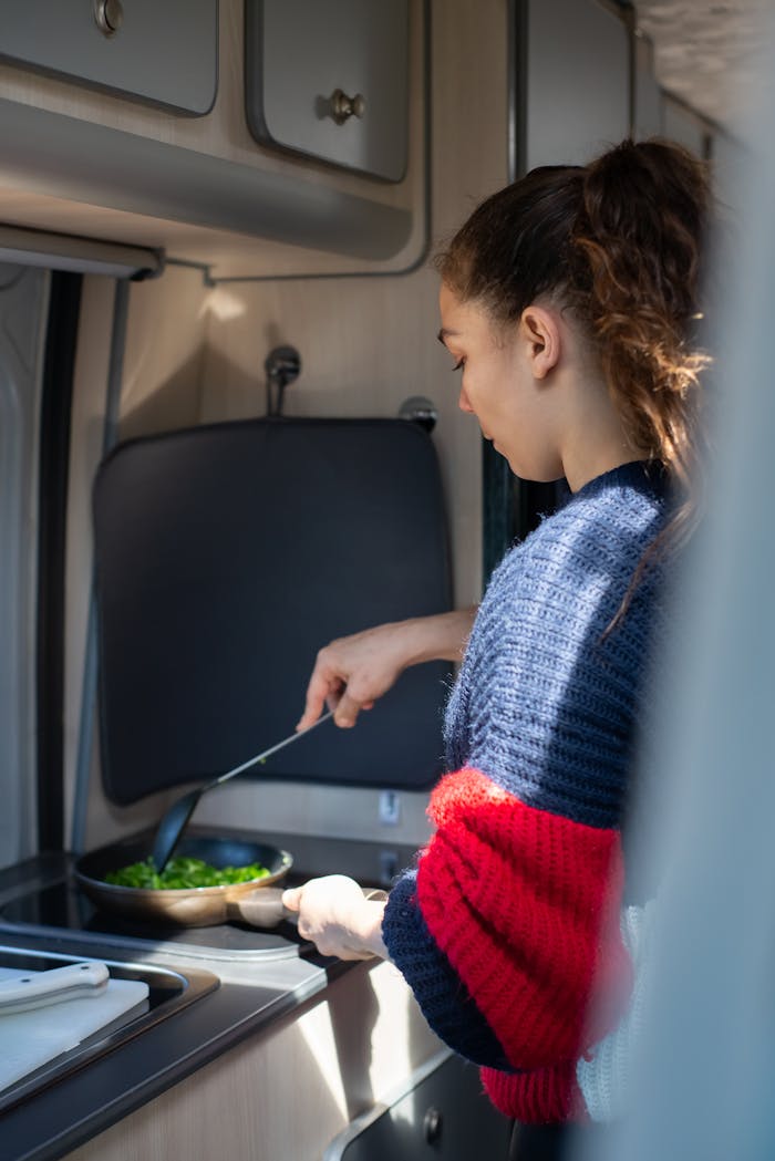 A woman prepares a meal in a camper van kitchen, highlighting van life.